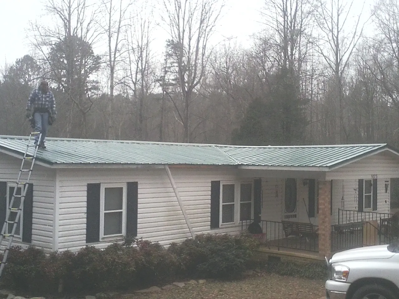 Worker on a ladder beside a new green metal roof on a ranch home in Newbury