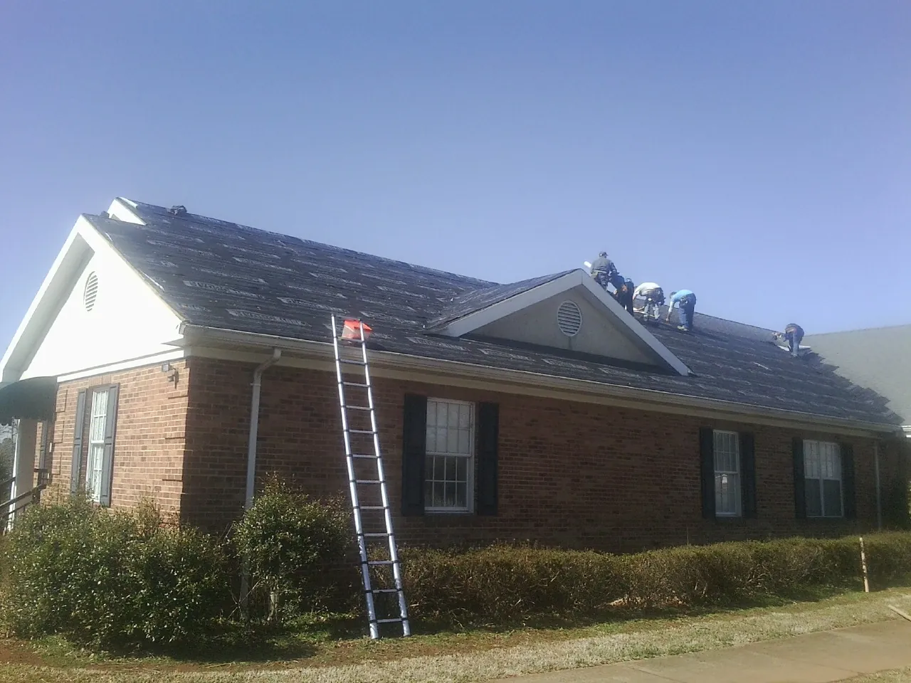 Crew tearing shingles off a brick ranch roof with a ladder set — Emergency Roof Repair work by our crew in Newbury