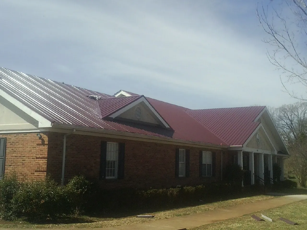 Red metal roof with gabled entries on a long brick building, from a Hail Damage Roof Repair job in Newbury