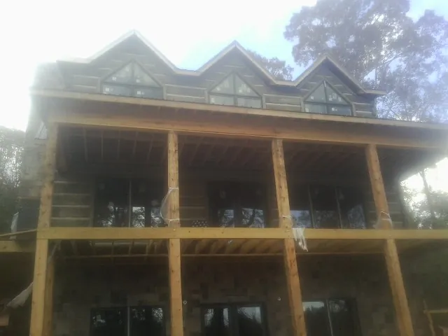 Dormers and porch framing on a large log home under construction — Roof Coating work by our crew in Newbury